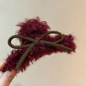 Detail view of a burgundy flocked hair claw clip with a plush texture and dark bow decoration