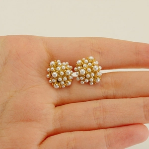 Detailed view of cluster pearl stud earrings with gold base held in hand for scale