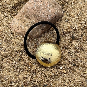 Golden brushed metal circle hair tie with black high elastic rope on desert rock