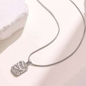 Macro detail of a silver rectangular pendant with hammered texture on a snake chain