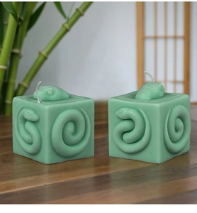 Detail of green square aromatherapy candles with 3D snake relief and bamboo backdrop