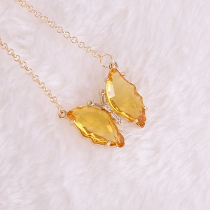 Close-up of golden butterfly necklace with yellow faceted gems on white plush background