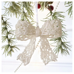 Close-up of glittery white and silver Christmas bow ornament hanging on a pine tree