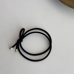 Détail d'un élastique à cheveux noir avec nœud minimaliste et embouts dorés