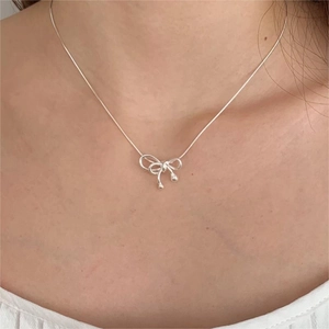 Detailed close-up of a sterling silver bow pendant necklace on a model's neck