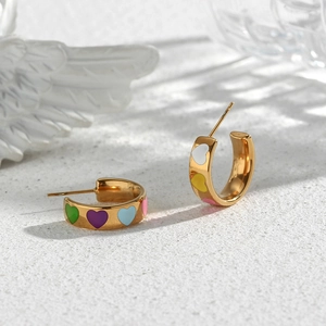Macro detail of gold C-shaped earrings with colorful heart-shaped enamel patterns
