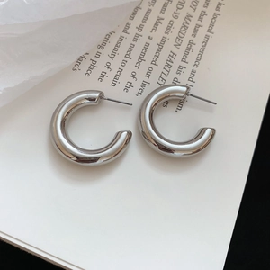 Polished silver C-shaped hoop earrings on a fashion magazine with a minimalist metallic glow