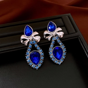 Detail shot of silver bow earrings with blue teardrop gemstones and sparkling crystals