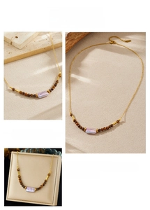 Detail of gold chain necklace featuring tiger eye beads and iridescent purple stone pendant