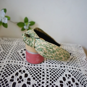 Close-up of green and beige woven raffia headband with knot on lace tablecloth