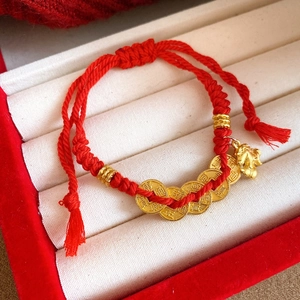 Detail of red braided bracelet with five emperor coins and a gold horse pendant in a gift box