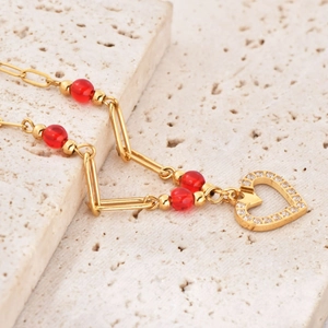 18k gold plated stainless steel heart necklace with red beads on stone background