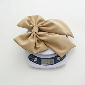 Detail view of khaki bow hair clip on a scale showing a precise weight of 31.4 grams