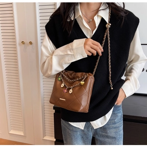 Quilted brown bucket bag featuring metal chain and colorful charms on model