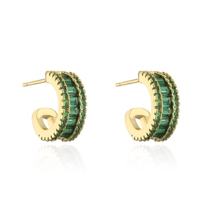 Detailed view of C-shaped gold earrings with emerald green zircons on a white reflective base