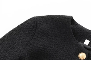 Close-up of black tweed fabric texture and decorative gold embossed button on the jacket