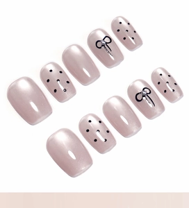 Detailed view of pink cat-eye press-on nails with black polka dots and tiny bows