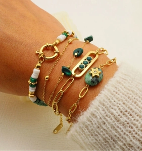 Detail of layered gold bracelets with green gemstones and star charm on woman's wrist