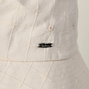 Macro view of cream embroidered check cotton bucket hat with metal brand logo tag