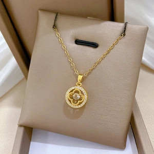 Detailed shot of golden four-leaf clover necklace with sparkling gems in a beige jewelry box