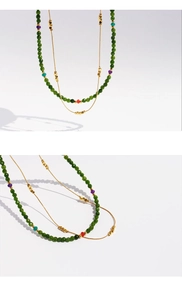 Close-up of layered gold chain necklace with green faceted beads and multicolor accents