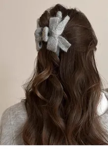 Detail of grey knitted bow hair claw clip styled on long brown wavy hair