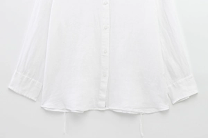 Detail of white long sleeve shirt showing fabric texture, buttons and hem tie knot