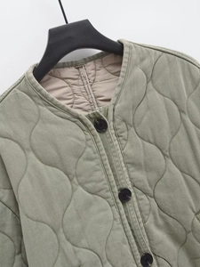 Détail du col rond et des boutons noirs d'une veste matelassée vert olive