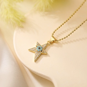 Gold plated copper necklace with star and blue evil eye pendant on a beige base