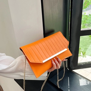 Elegant orange pleated clutch bag with gold trim and chain strap held by a model