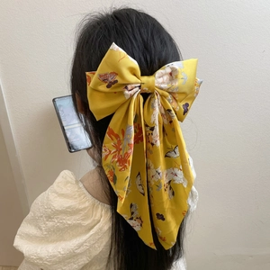 Large yellow satin bow hair clip with floral print on woman's hair back view