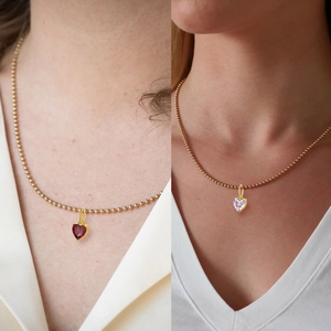 Close-up of small heart-shaped zircon pendants on gold bead chains in red and clear