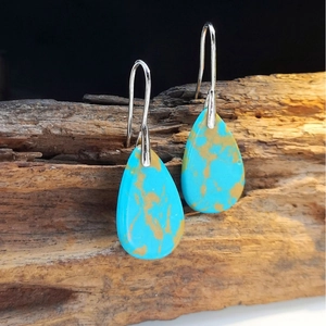 Macro detail of teardrop turquoise earrings with golden veins on vintage wood