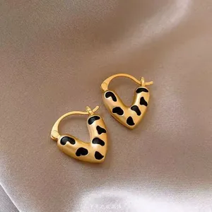Macro detail of heart-shaped gold earrings with black animal print on satin fabric