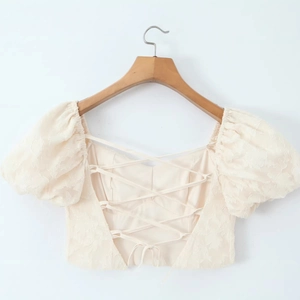 Top corto off-white con maniche a sbuffo, trama jacquard e design incrociato sul retro