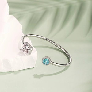 Detail of silver spring bangle featuring square zircon and blue gemstone on rock