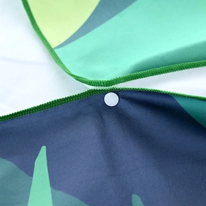 Detail of quick-dry beach towel featuring green edge stitching and a white snap button