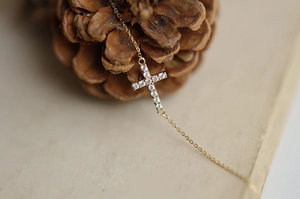 Macro shot of a gold cross necklace with pavé-set stones on vintage paper and pinecone