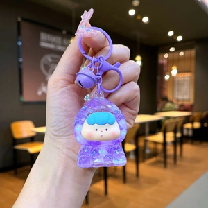 Détail d'un porte-clés astronaute violet avec effet sable mouvant pailleté et cloche