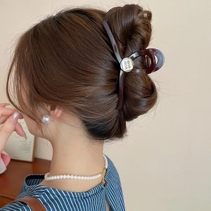 Deep burgundy acrylic hair claw clip with metallic logo detail worn on a model hair