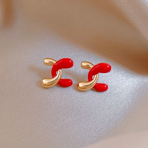 Detail of elegant red and gold twisted stud earrings on a luxury silk fabric background