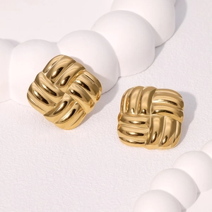 Golden geometric square earrings with woven texture on a white decorative pedestal