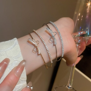 Close-up of zircon bow cuff bracelets and diamond-encrusted bangles in gold and silver