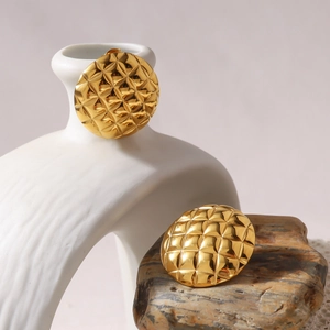 Detailed view of golden round quilted earrings on a white vase and natural stone backdrop