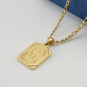 Macro shot of gold 18K stainless steel square letter M pendant with Figaro chain detail