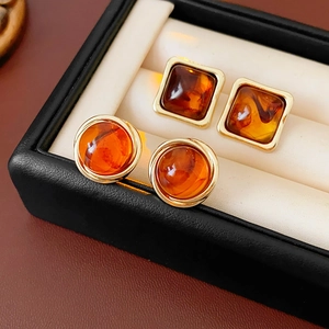 Detail of round and square amber resin earrings in gold metal bases on black box