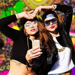 Women wearing oversized sunglasses with gold hip-hop jewelry set against graffiti wall