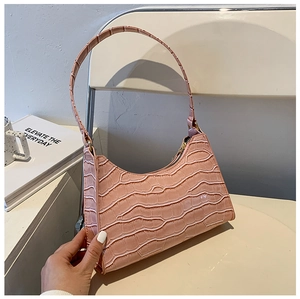 Detail of pink crocodile embossed shoulder bag with gold zipper on a minimalist chair