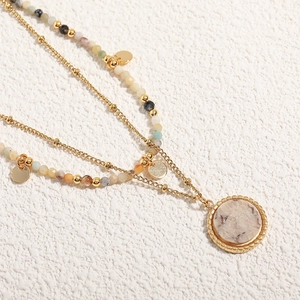 Layered gold-plated necklace with colorful beads and textured round pendant on white surface