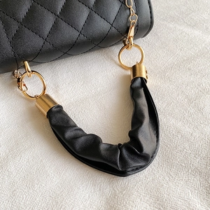 Detalle de bolso negro en piel sintética con asa fruncida, acolchado y aros dorados